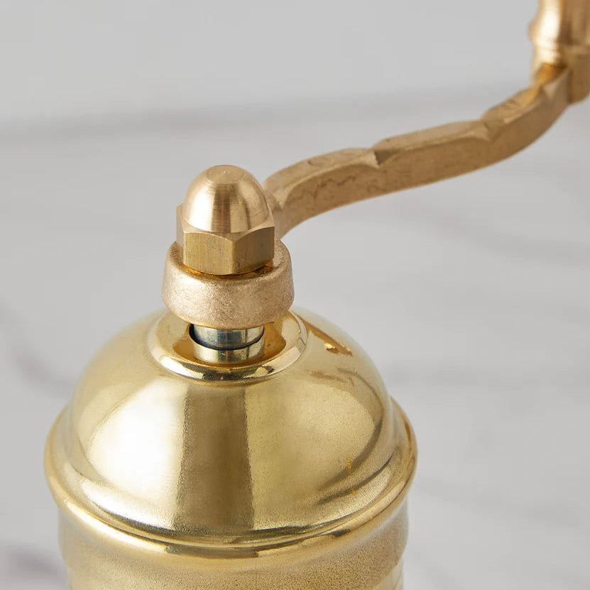 Brass pepper grinder with intricate patterns on a light gray background