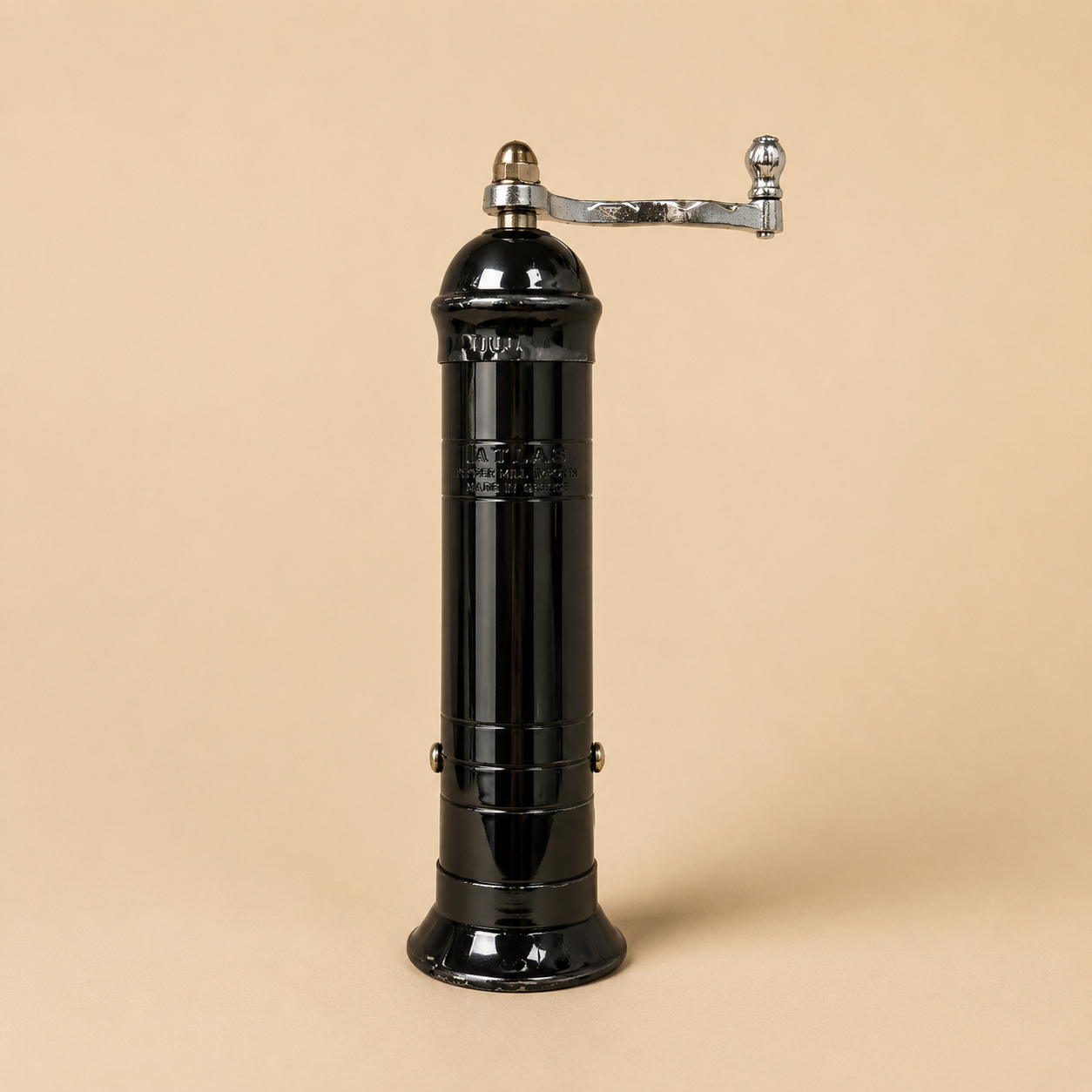 Atlas Black Pepper Mill handmade in Greece featuring a glossy black metal body, polished chrome handle, and beige studio background. Traditional manual pepper grinder with durable metal grinding mechanism.