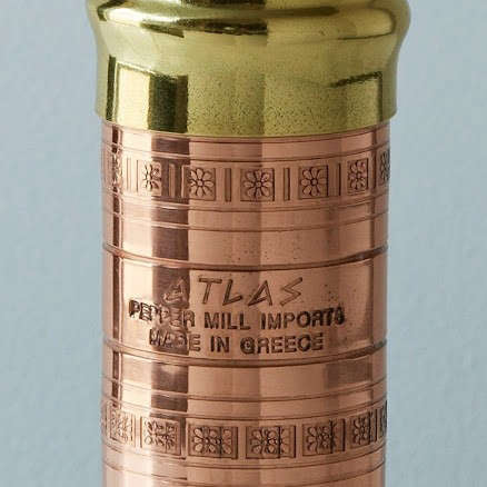 Copper pepper mill with gold top on a light gray background