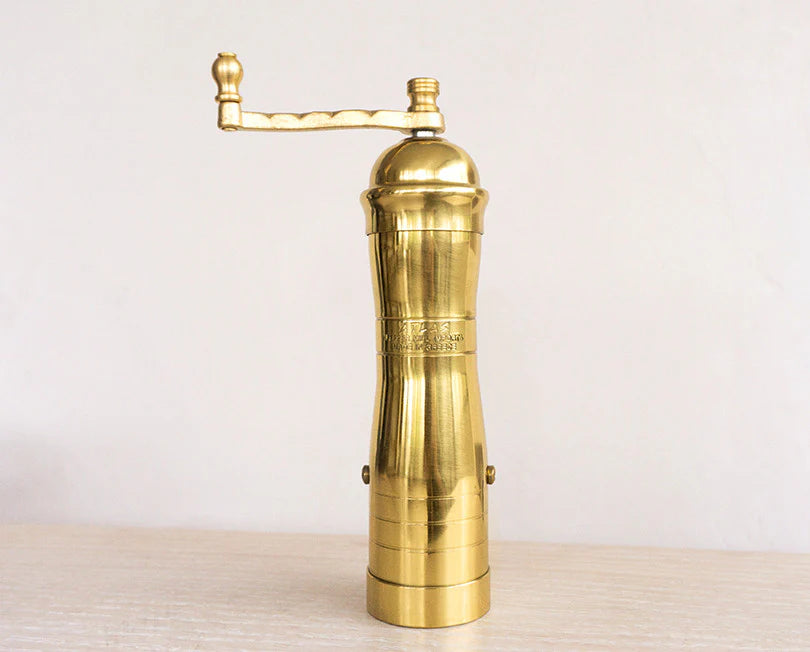 Gold pepper grinder on a light wooden surface with a white background