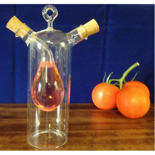 Glass distillation apparatus with liquid and cork stoppers on a wooden surface with tomatoes in the background.