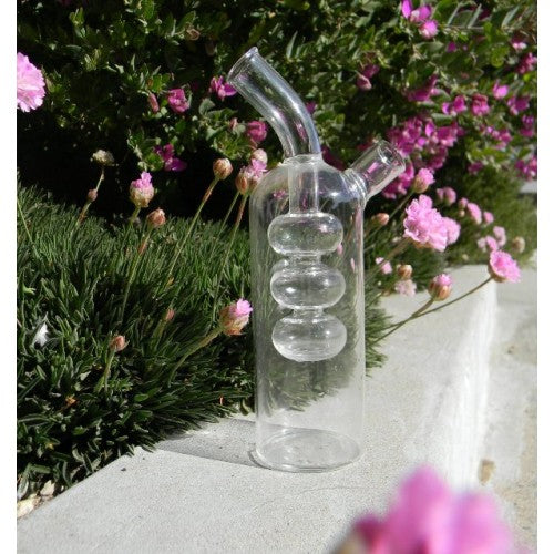 Clear glass water pipe with spiral design on a concrete surface with flowers in the background