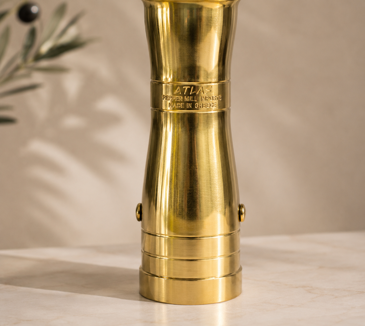 Brass pepper mill with 'Atlas' branding on a beige background