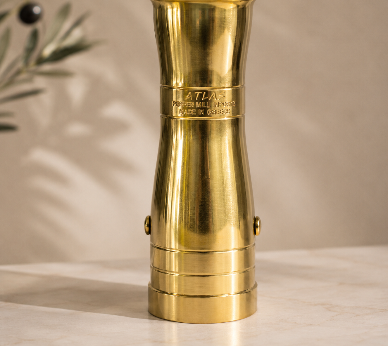 Brass pepper mill with 'Atlas' branding on a beige background