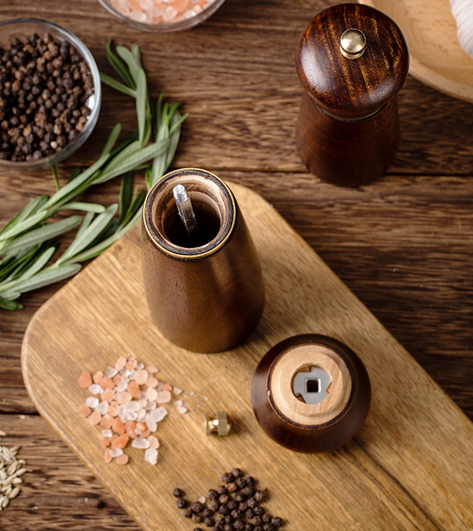 Wooden pepper grinder and mill on a wooden surface with herbs and spices.