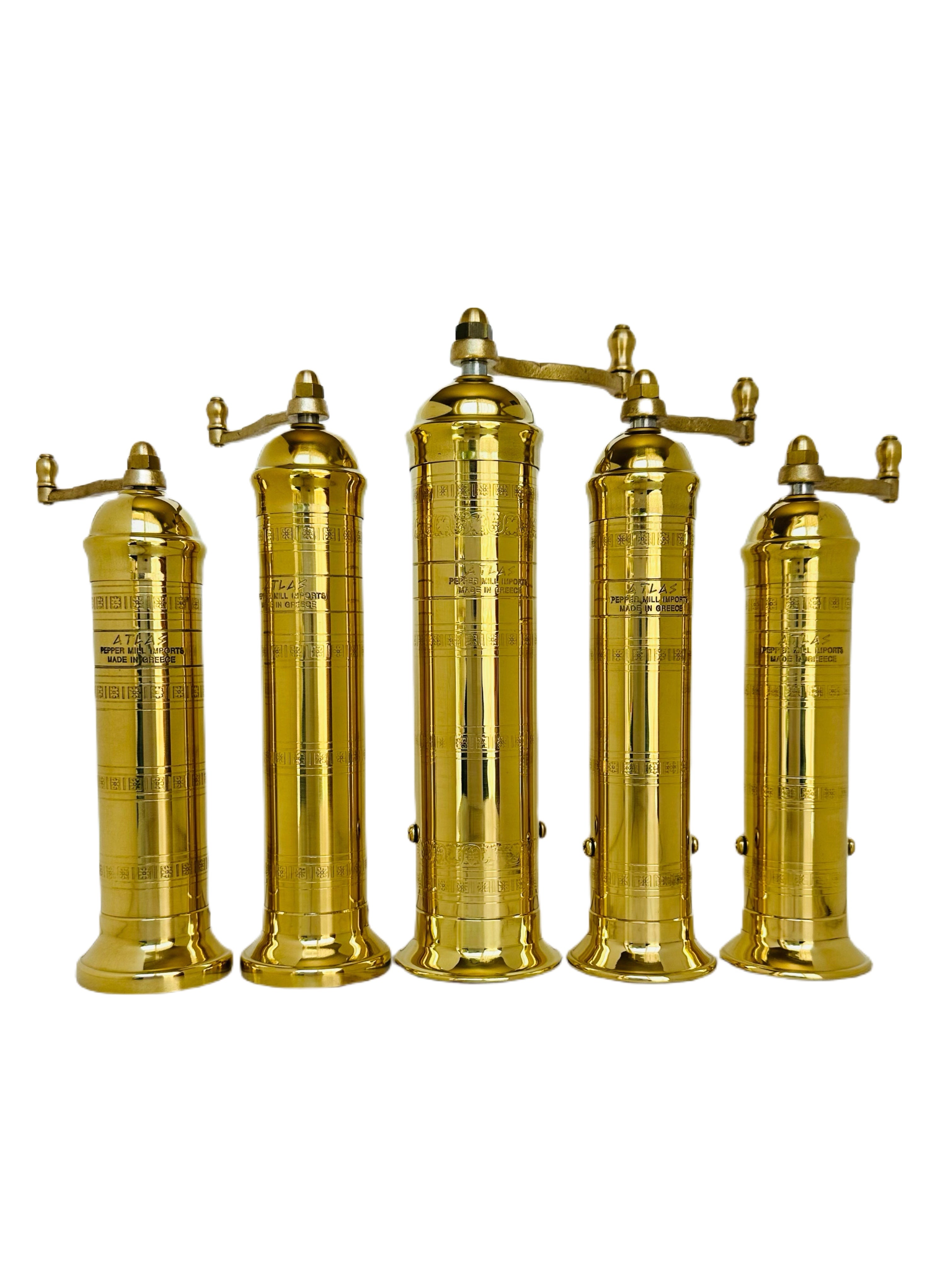 Set of five brass pepper grinders on a white background