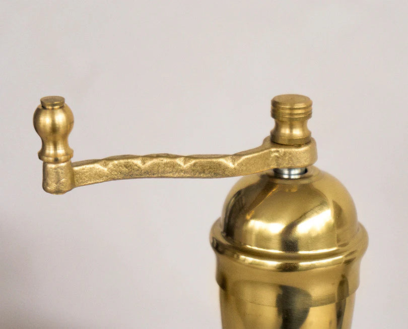 Brass manual coffee grinder on a light gray background