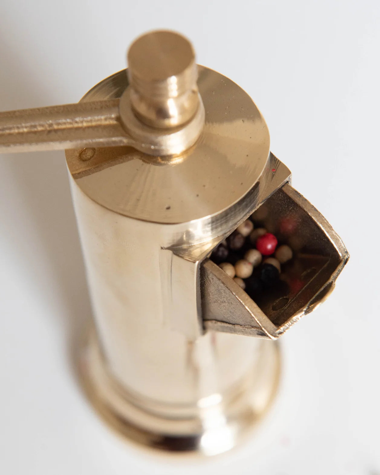 Elegant gold Atlas Pepper Mill surrounded by scattered pepper flakes.