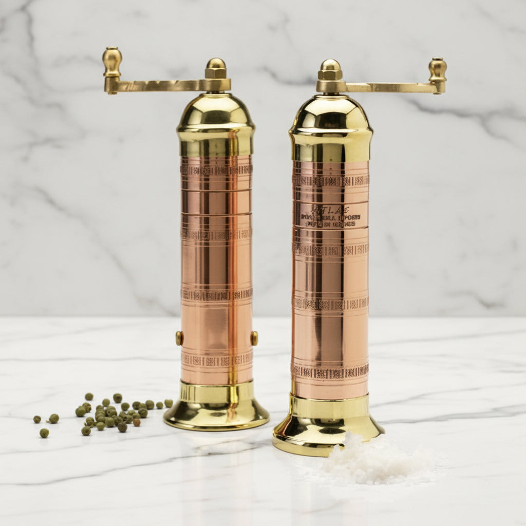 Two brass pepper mills with a small amount of pepper and salt on a white background