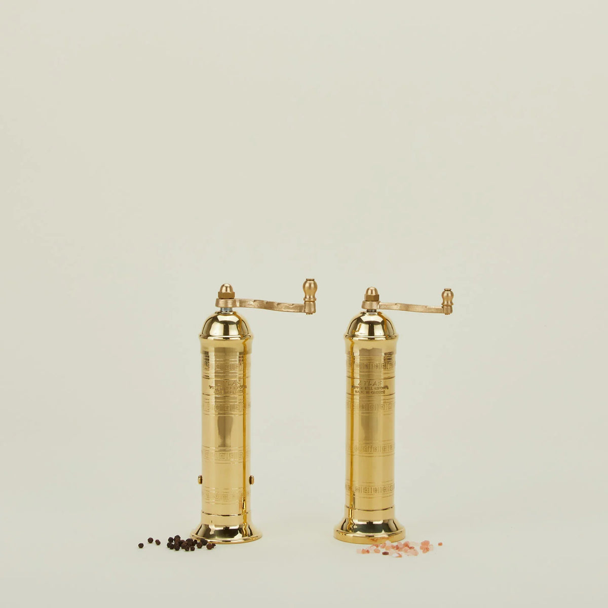 Pair of gold pepper mills on a light beige background
