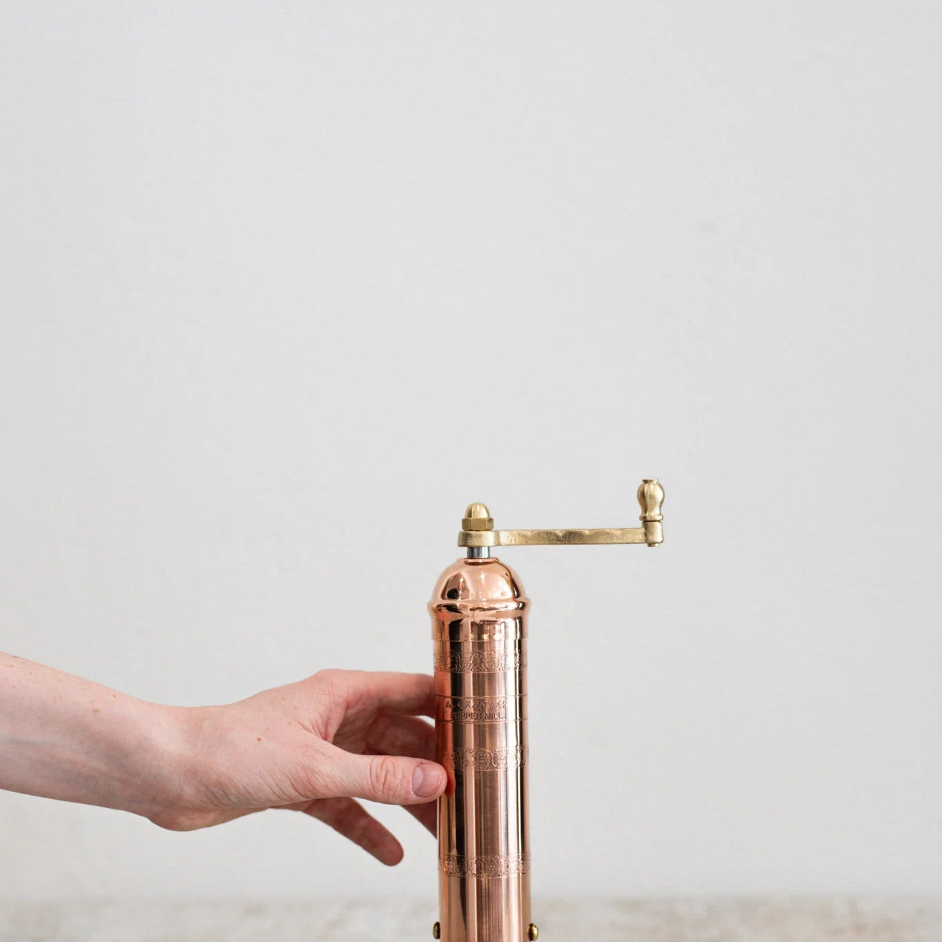 Copper pepper grinder held by a hand on a light background