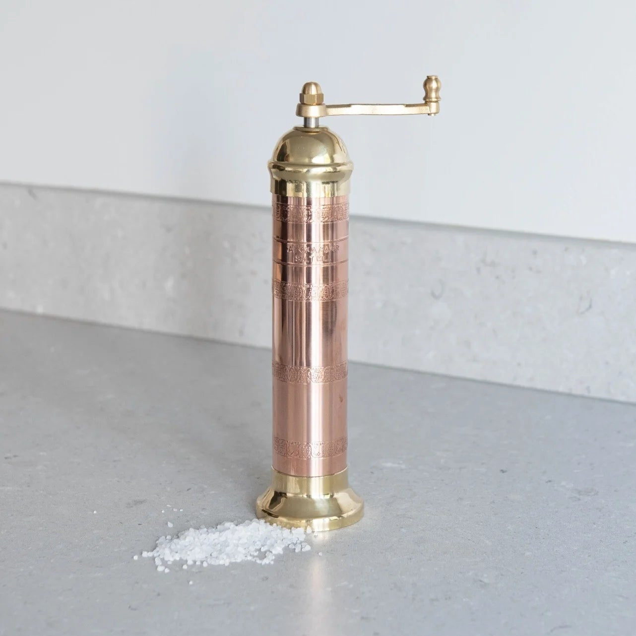 Copper and brass pepper grinder on a gray surface with a white background