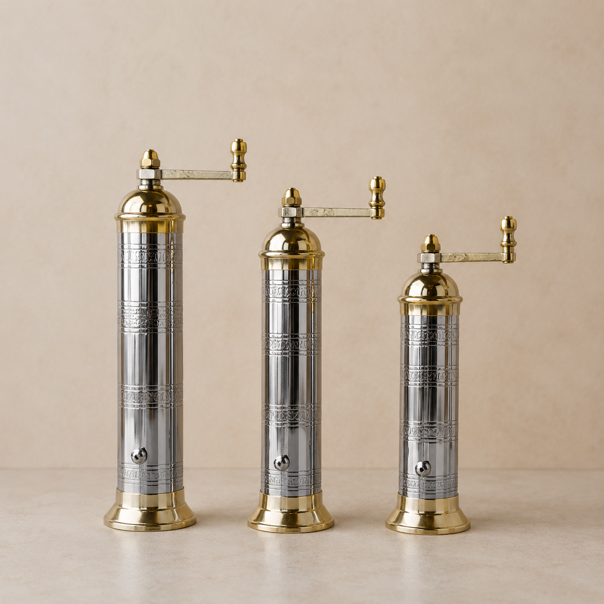 Three gold and silver pepper mills on a beige background
