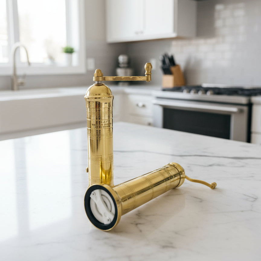 Gold-colored brass pepper and salt mill set a marble countertop in a kitchen